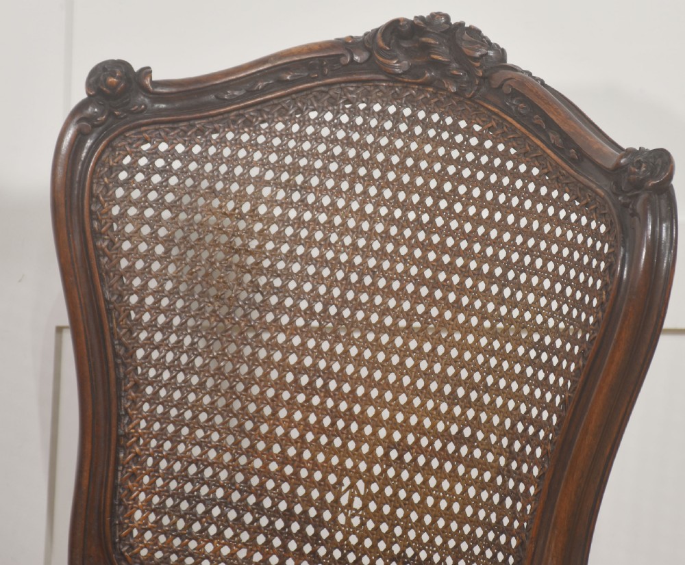 A pair of carved walnut side chairs in the Louis XV style, featuring woven cane backs, dark leather button-tufted seats, and cabriole legs. View III