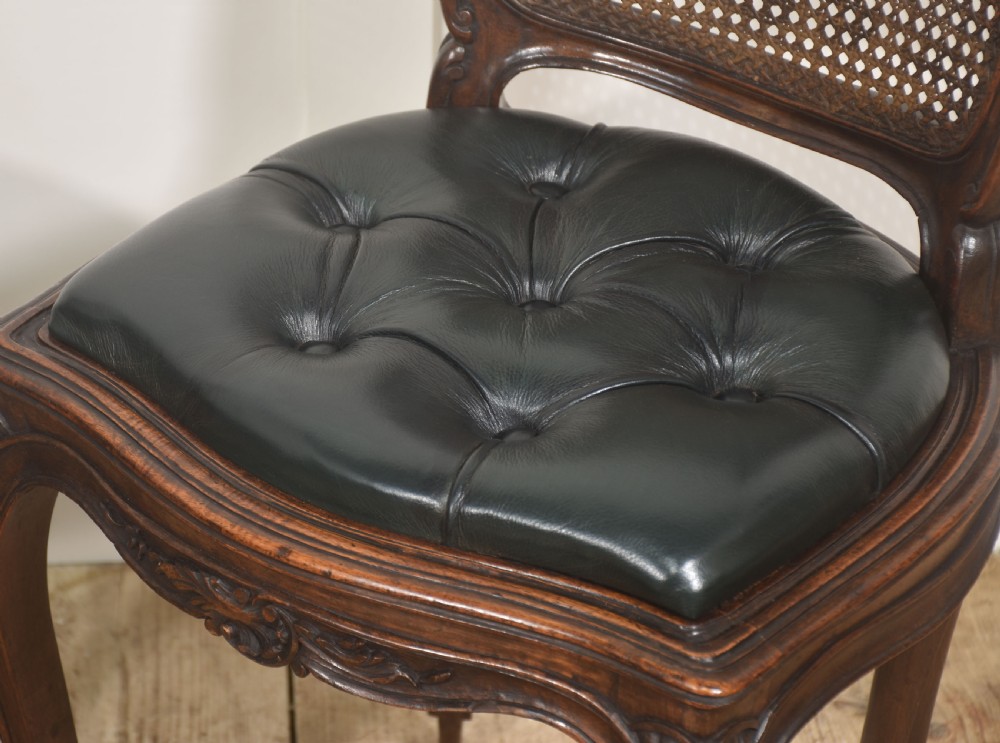 A pair of carved walnut side chairs in the Louis XV style, featuring woven cane backs, dark leather button-tufted seats, and cabriole legs. View VII