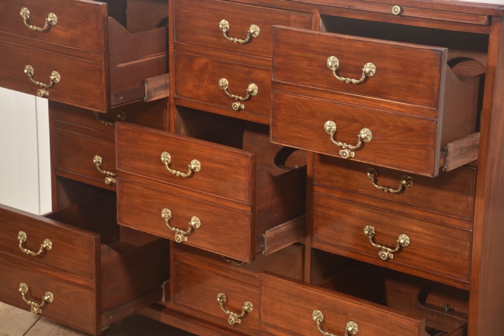 A Georgian style mahogany filing cabinet featuring a bank of multiple small drawers with brass swan-neck handles on a bracket foot base. View XII
