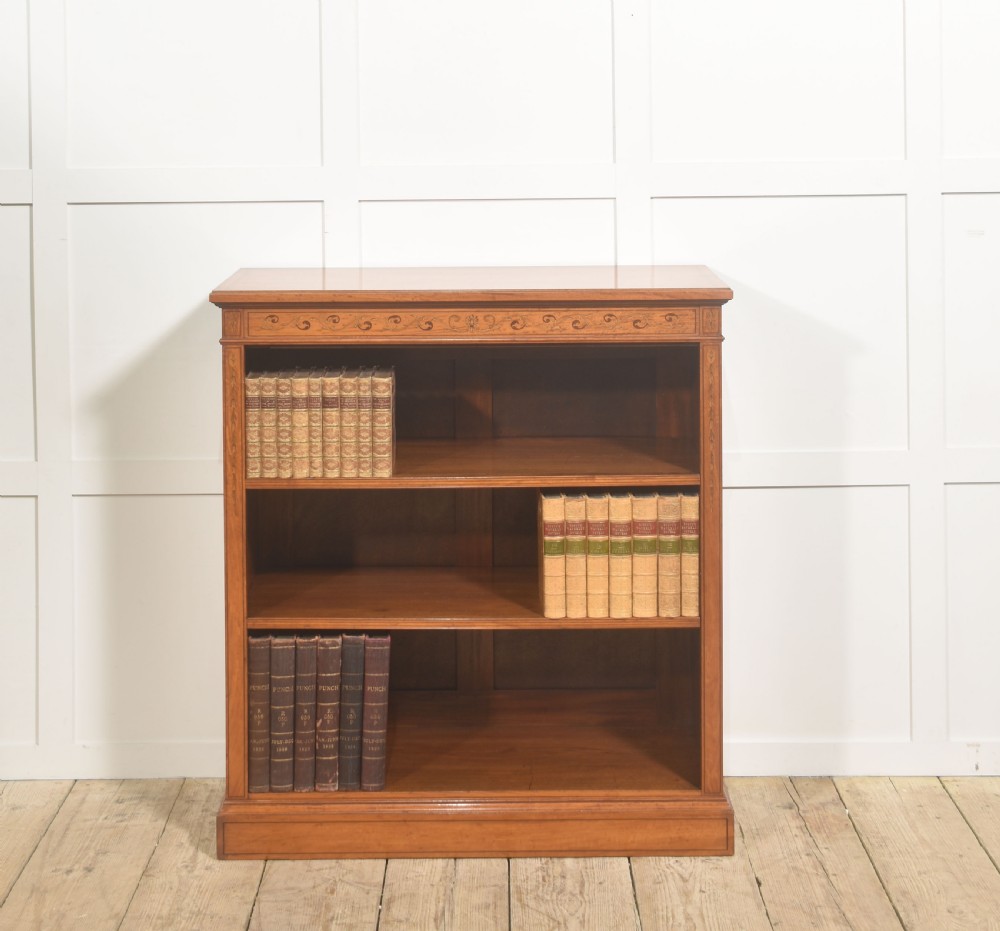 A low satinwood open bookcase featuring three shelves and a decorative inlaid floral frieze across the top.