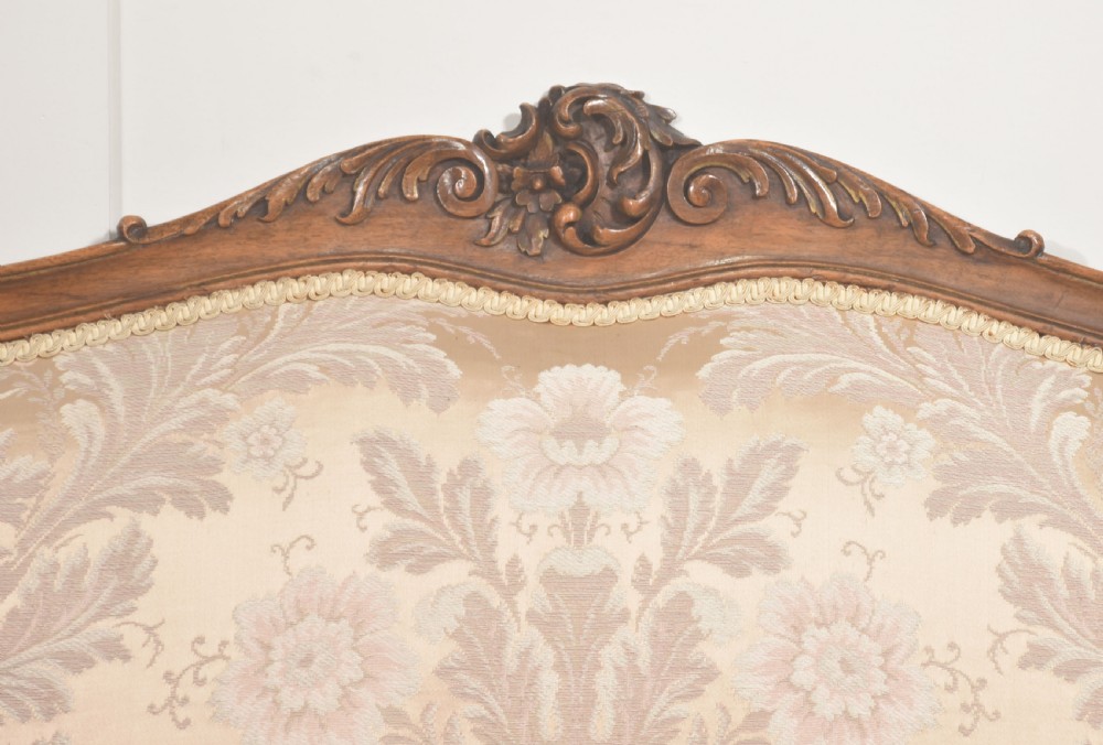 A Louis XV style carved walnut settee upholstered in beige damask fabric, featuring cabriole legs, padded armrests, and a carved cresting rail. View II