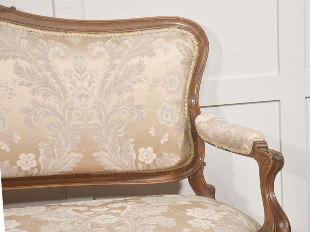 A Louis XV style carved walnut settee upholstered in beige damask fabric, featuring cabriole legs, padded armrests, and a carved cresting rail. View III