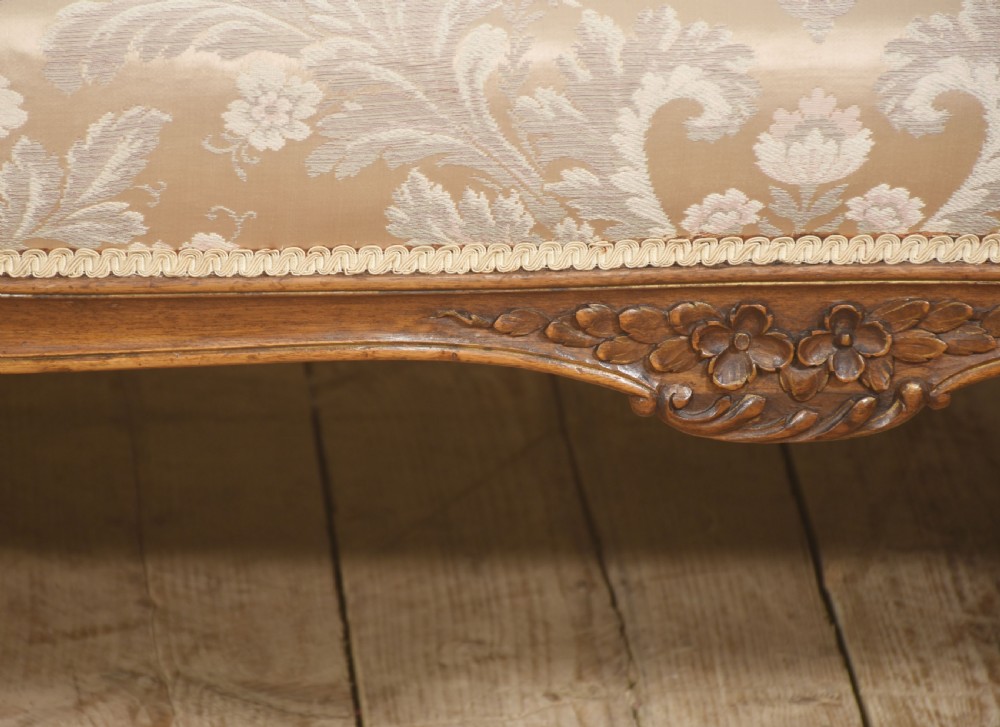 A Louis XV style carved walnut settee upholstered in beige damask fabric, featuring cabriole legs, padded armrests, and a carved cresting rail. View IV