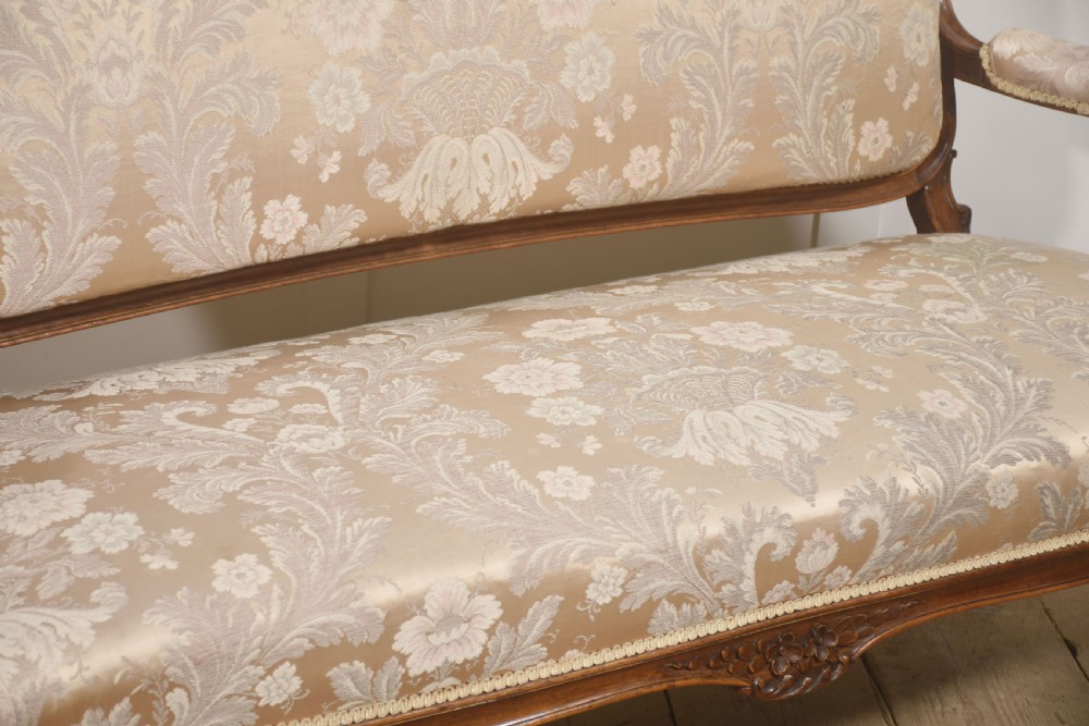 A Louis XV style carved walnut settee upholstered in beige damask fabric, featuring cabriole legs, padded armrests, and a carved cresting rail. View VI