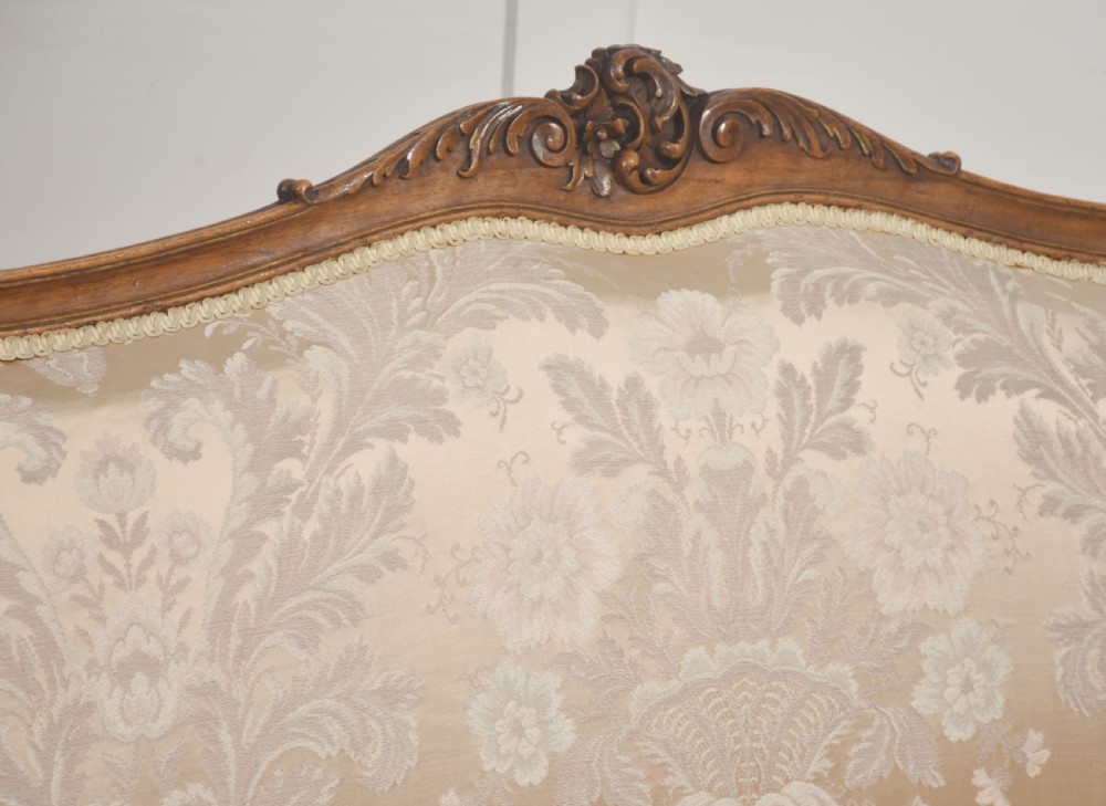 A Louis XV style carved walnut settee upholstered in beige damask fabric, featuring cabriole legs, padded armrests, and a carved cresting rail. View VIII