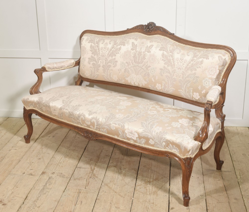 A Louis XV style carved walnut settee upholstered in beige damask fabric, featuring cabriole legs, padded armrests, and a carved cresting rail. View IX