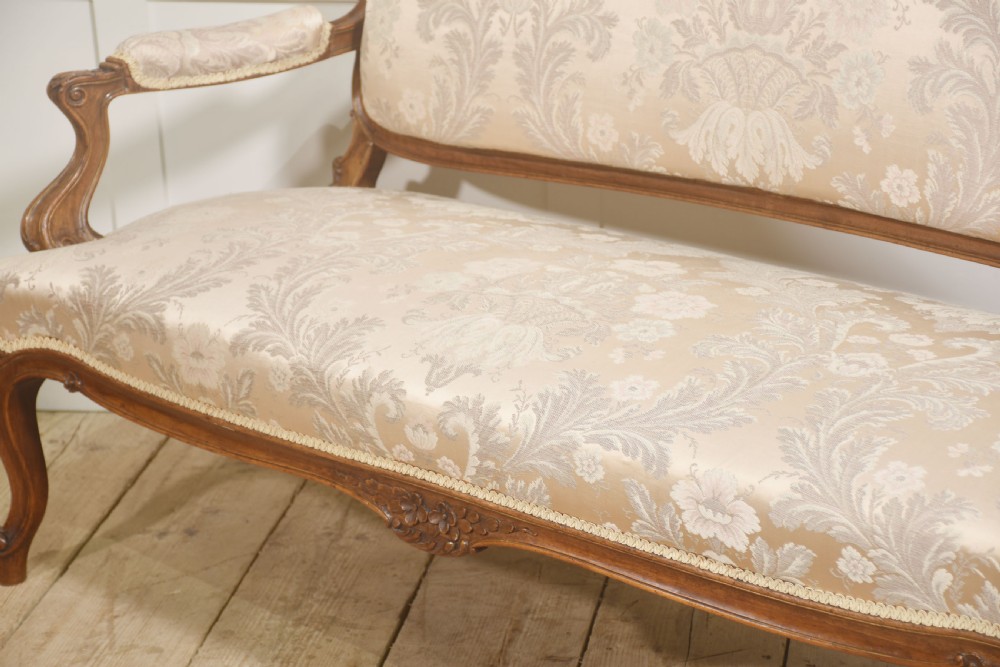 A Louis XV style carved walnut settee upholstered in beige damask fabric, featuring cabriole legs, padded armrests, and a carved cresting rail. View XII