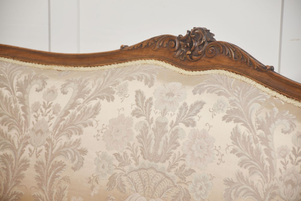 A Louis XV style carved walnut settee upholstered in beige damask fabric, featuring cabriole legs, padded armrests, and a carved cresting rail. View XIII