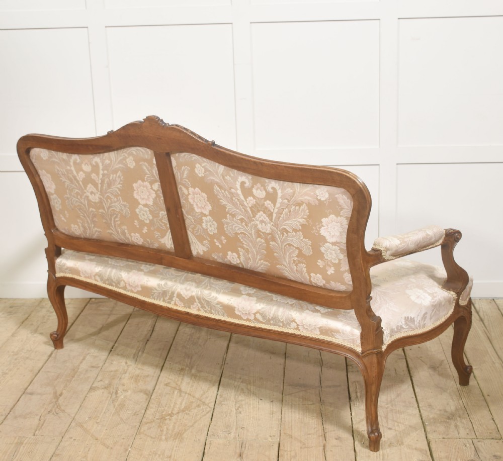 A Louis XV style carved walnut settee upholstered in beige damask fabric, featuring cabriole legs, padded armrests, and a carved cresting rail. View XIV