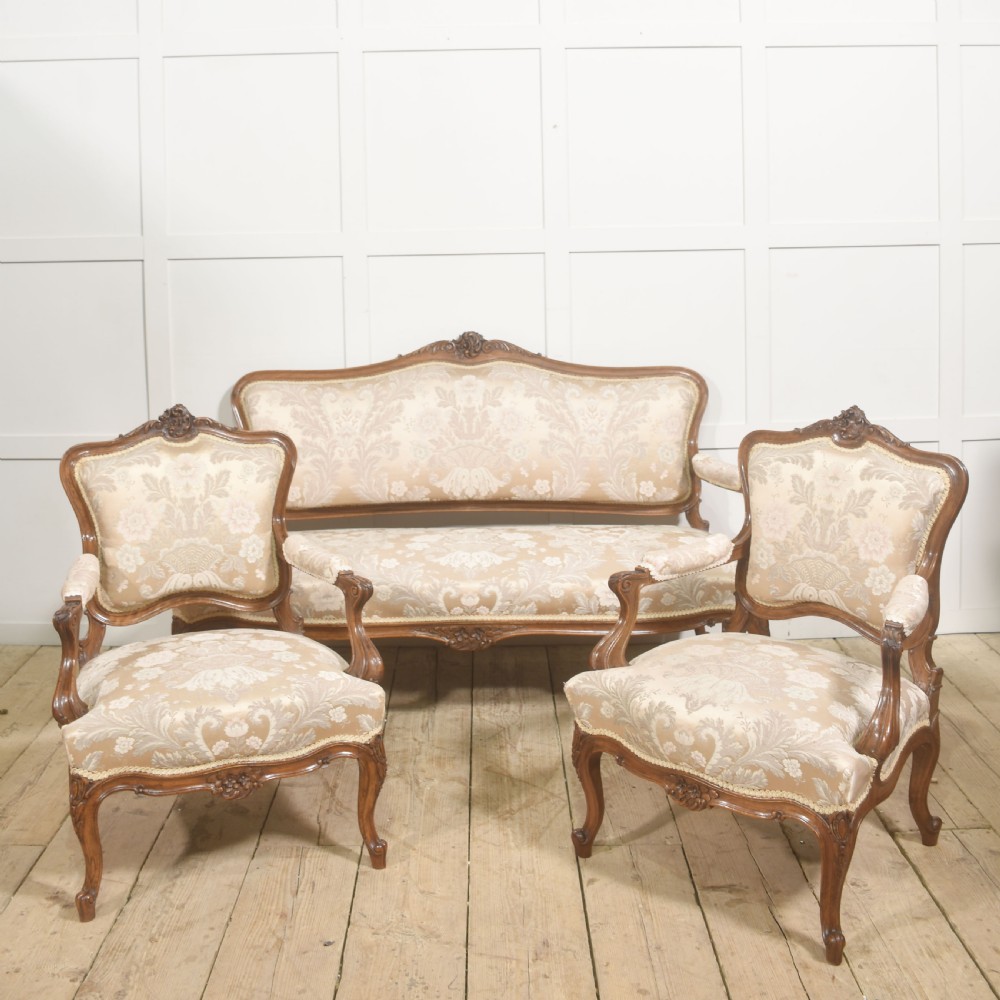 A Louis XV style carved walnut settee upholstered in beige damask fabric, featuring cabriole legs, padded armrests, and a carved cresting rail. View XV
