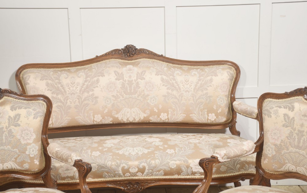 A Louis XV style carved walnut settee upholstered in beige damask fabric, featuring cabriole legs, padded armrests, and a carved cresting rail. View XVI