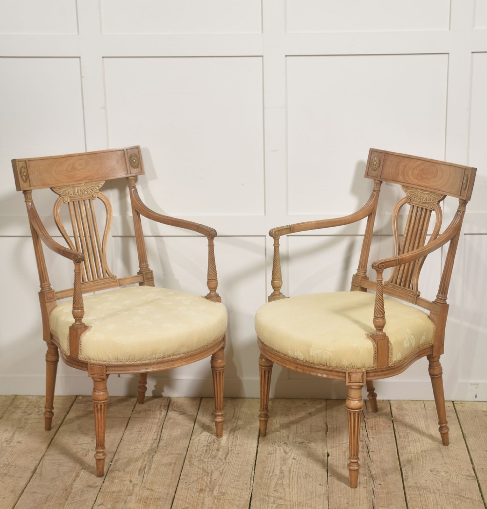 A pair of light mahogany open armchairs featuring lyre-designed back splats, carved rosettes on the top rails, fluted turned legs, and cream-patterned upholstered seats.