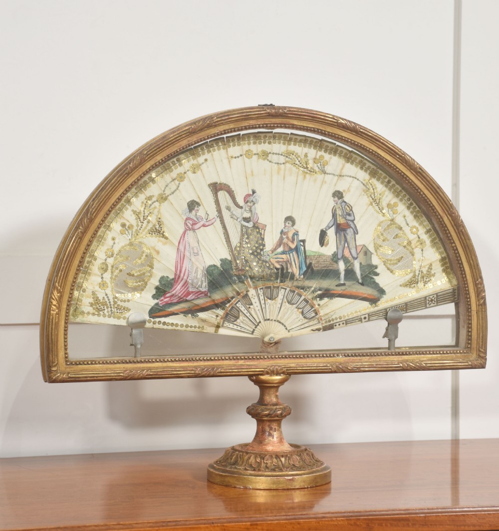 A hand-painted folding fan featuring a pastoral musical scene mounted inside a glazed giltwood frame on a turned pedestal. View IV