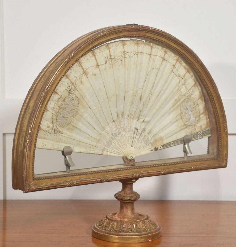 A hand-painted folding fan featuring a pastoral musical scene mounted inside a glazed giltwood frame on a turned pedestal. View VI