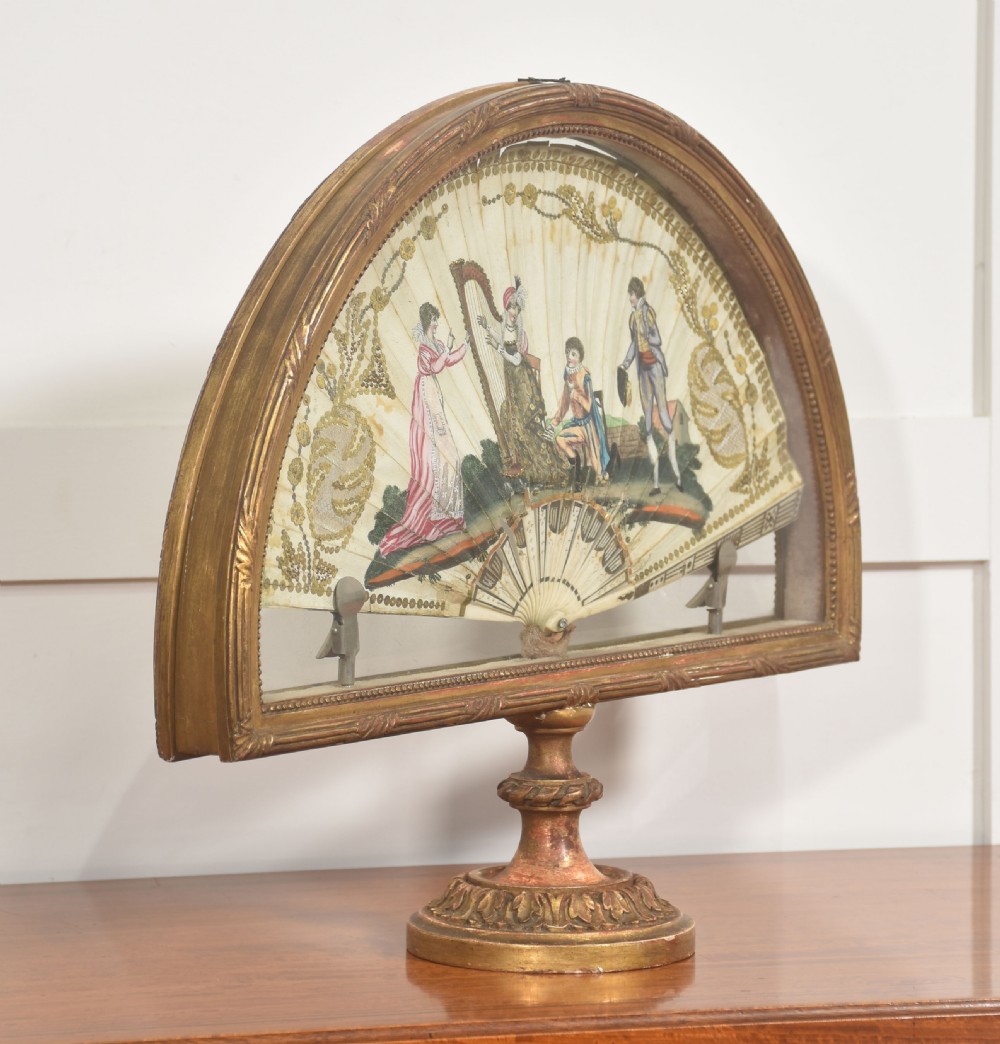 A hand-painted folding fan featuring a pastoral musical scene mounted inside a glazed giltwood frame on a turned pedestal. View VII