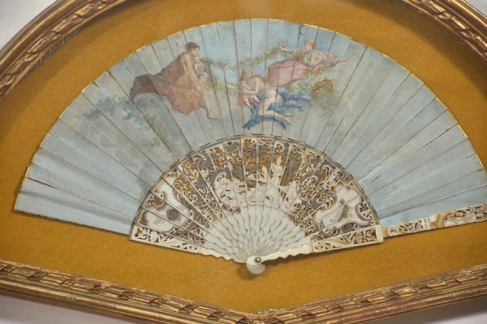 A nineteenth-century hand-painted fan depicting classical figures, mounted inside a fan-shaped gilt wood frame against an ochre background. View II