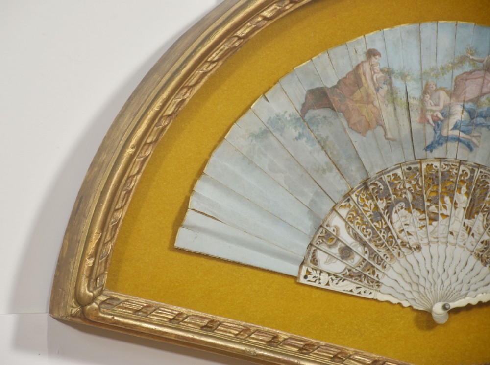 A nineteenth-century hand-painted fan depicting classical figures, mounted inside a fan-shaped gilt wood frame against an ochre background. View III