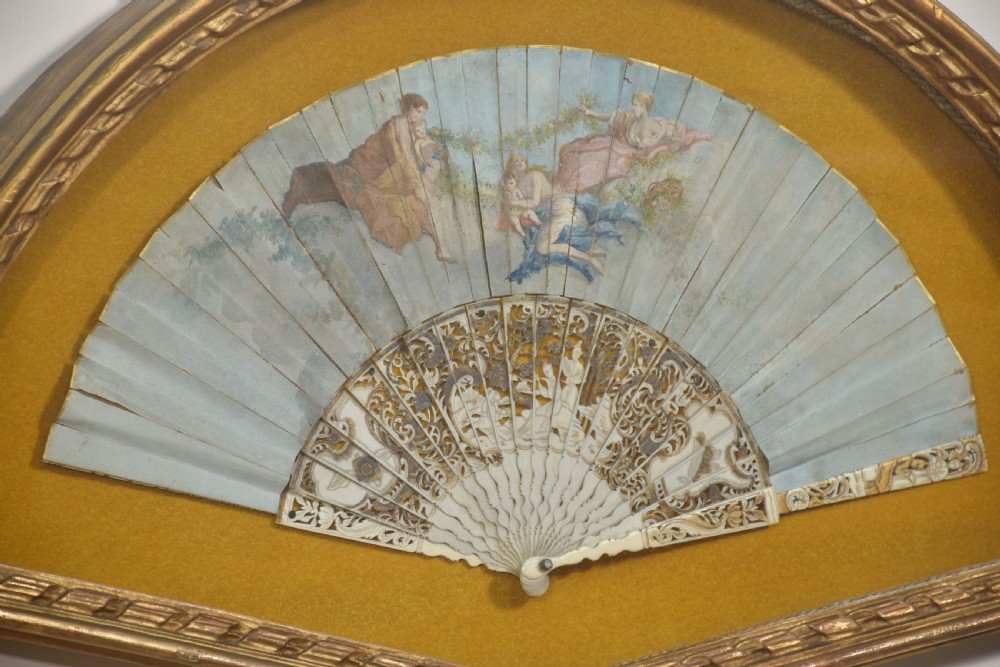 A nineteenth-century hand-painted fan depicting classical figures, mounted inside a fan-shaped gilt wood frame against an ochre background. View V