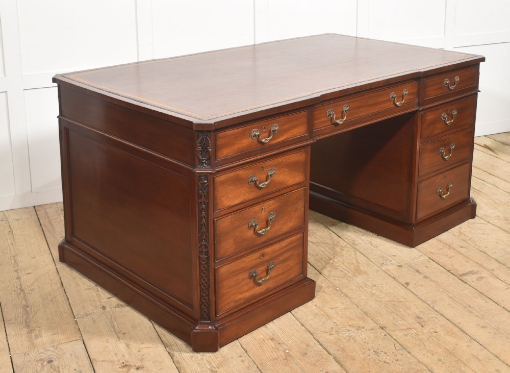 A large mahogany pedestal desk featuring a leather writing surface, multiple drawers with brass swan-neck handles, and carved corner details.