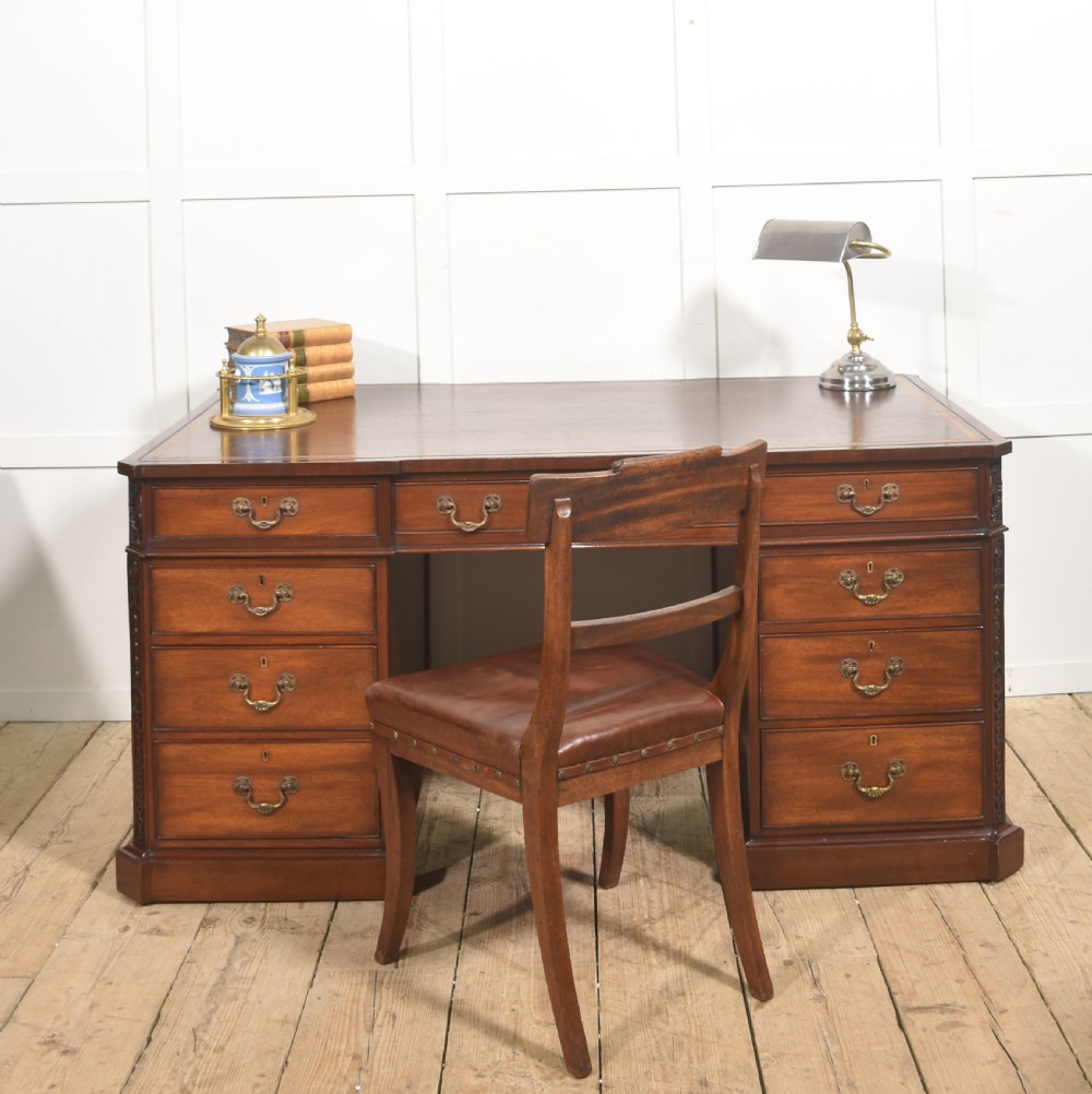 A large mahogany pedestal desk featuring a leather writing surface, multiple drawers with brass swan-neck handles, and carved corner details. View II