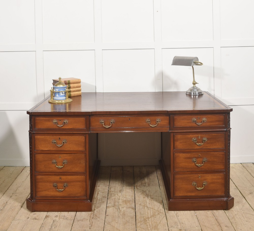 A large mahogany pedestal desk featuring a leather writing surface, multiple drawers with brass swan-neck handles, and carved corner details. View III
