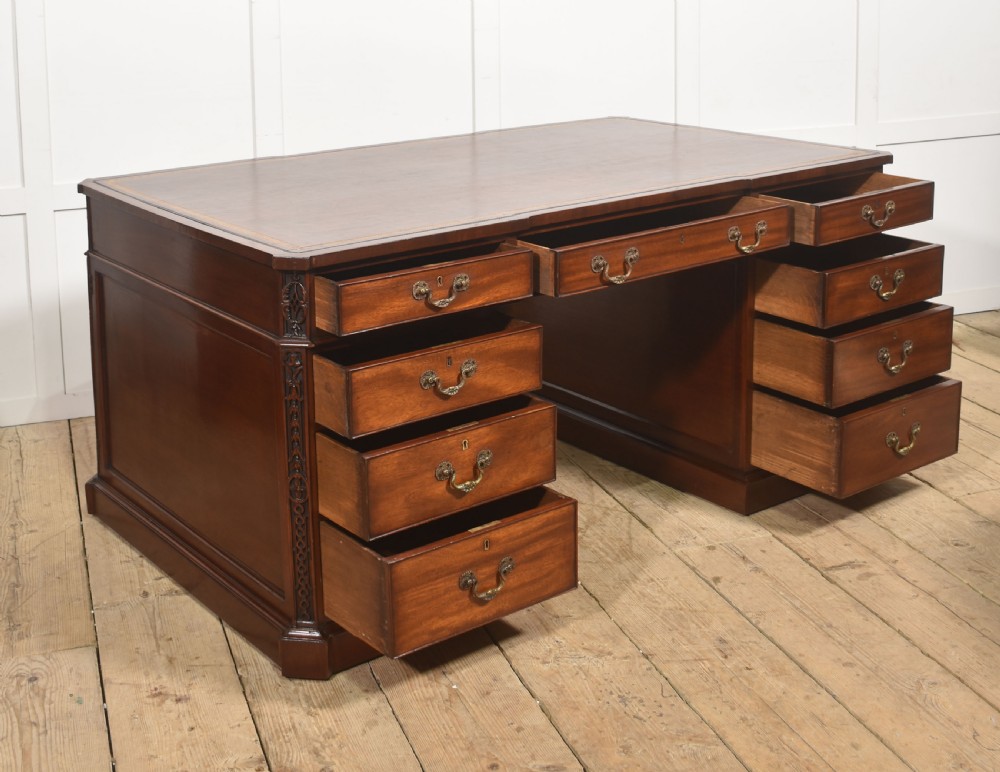 A large mahogany pedestal desk featuring a leather writing surface, multiple drawers with brass swan-neck handles, and carved corner details. View VI