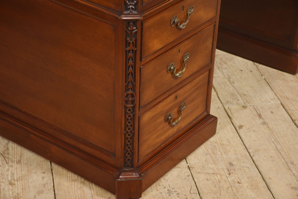 A large mahogany pedestal desk featuring a leather writing surface, multiple drawers with brass swan-neck handles, and carved corner details. View X