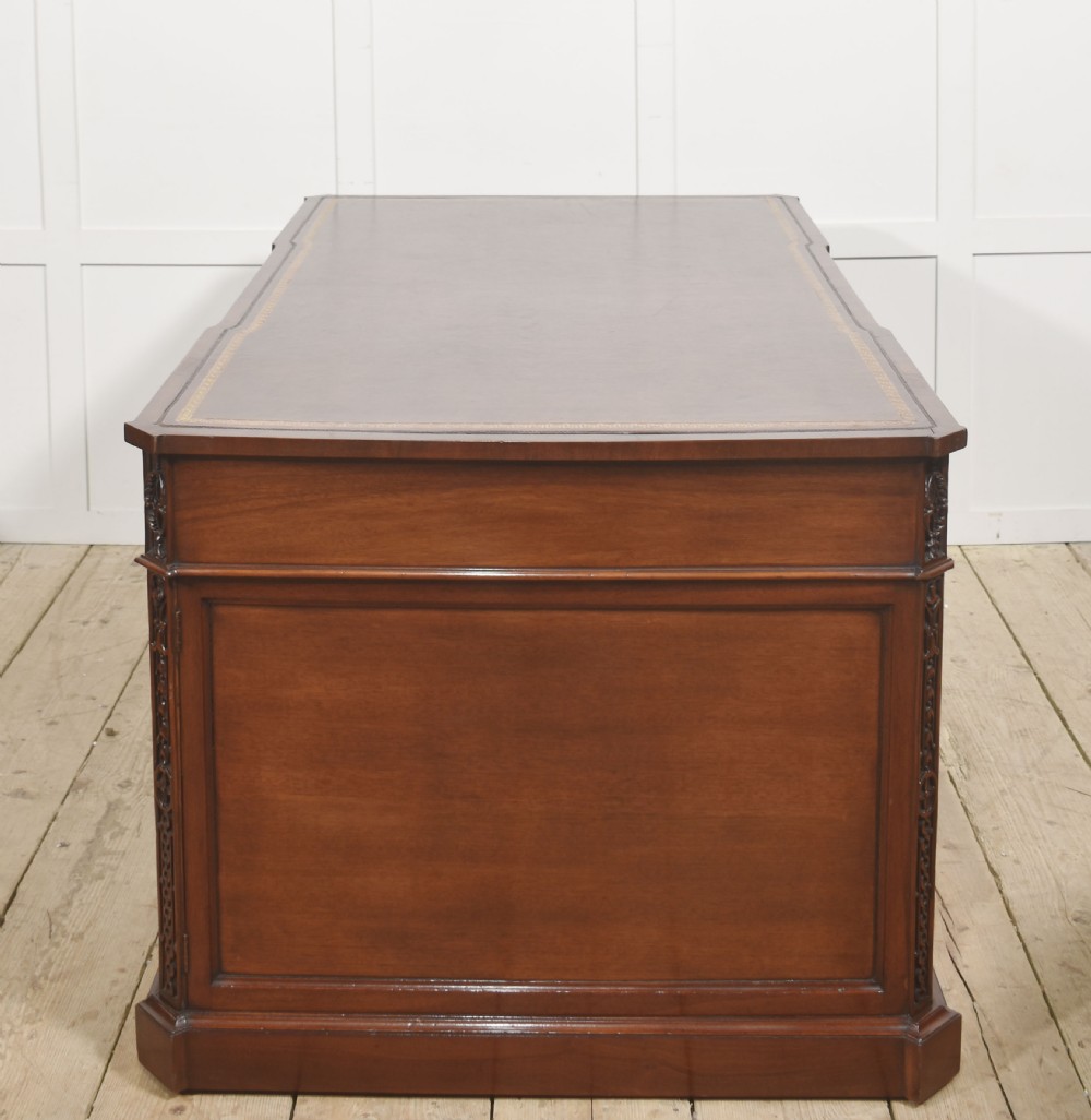A large mahogany pedestal desk featuring a leather writing surface, multiple drawers with brass swan-neck handles, and carved corner details. View XI