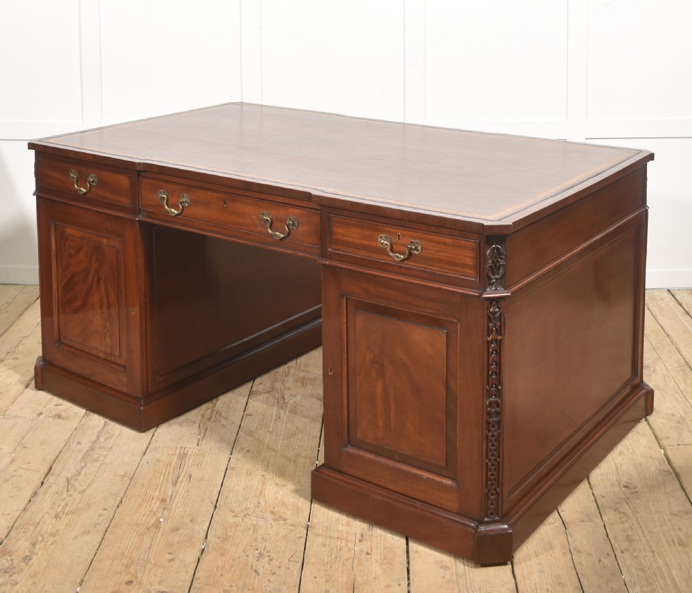A large mahogany pedestal desk featuring a leather writing surface, multiple drawers with brass swan-neck handles, and carved corner details. View XII