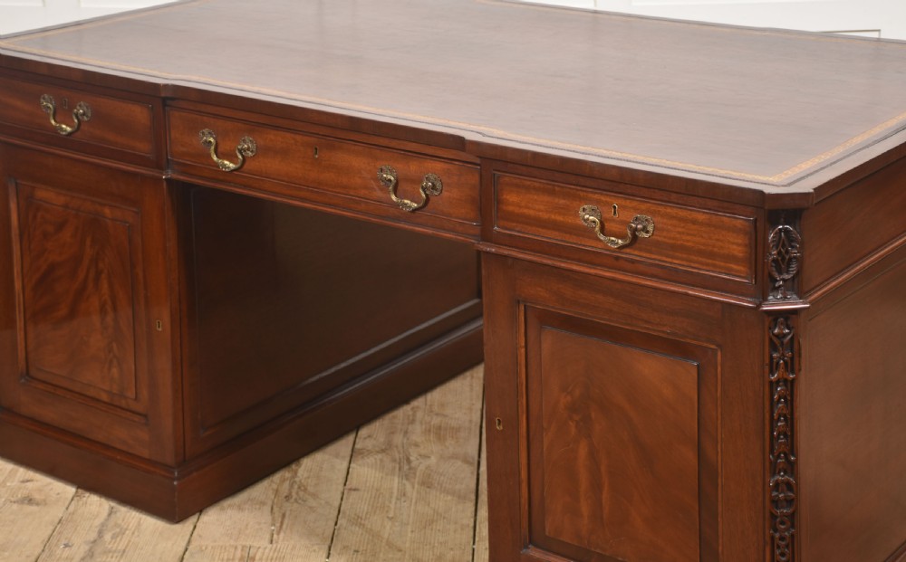 A large mahogany pedestal desk featuring a leather writing surface, multiple drawers with brass swan-neck handles, and carved corner details. View XIII