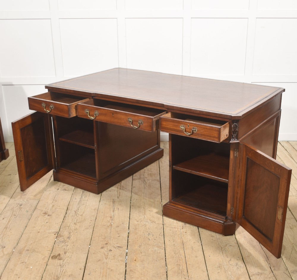 A large mahogany pedestal desk featuring a leather writing surface, multiple drawers with brass swan-neck handles, and carved corner details. View XIV