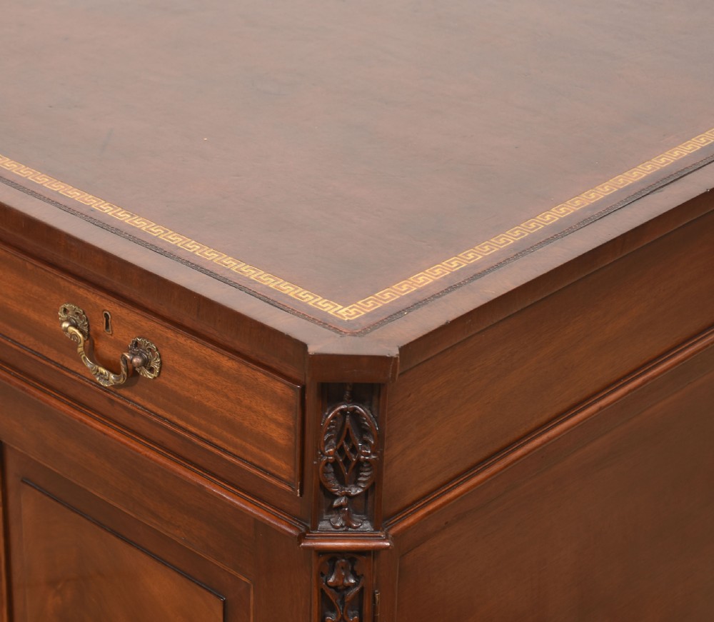 A large mahogany pedestal desk featuring a leather writing surface, multiple drawers with brass swan-neck handles, and carved corner details. View XV