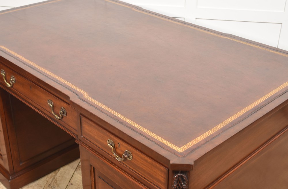 A large mahogany pedestal desk featuring a leather writing surface, multiple drawers with brass swan-neck handles, and carved corner details. View XVI