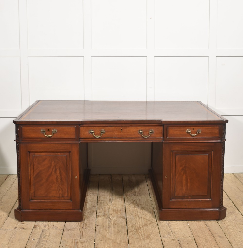 A large mahogany pedestal desk featuring a leather writing surface, multiple drawers with brass swan-neck handles, and carved corner details. View XVII