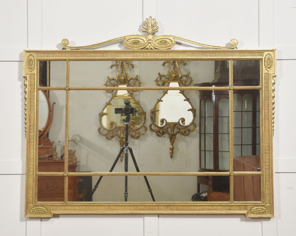 A horizontal Neoclassical giltwood panelled overmantel mirror featuring a top palmette crest, fluted frame, and sectioned glass plates.