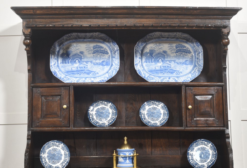 An antique dark oak Welsh dresser featuring an upper open shelf rack with two small side cupboards over a three-drawer base with two arched panel doors. View III