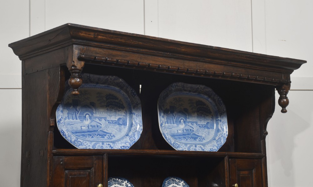 An antique dark oak Welsh dresser featuring an upper open shelf rack with two small side cupboards over a three-drawer base with two arched panel doors. View VIII