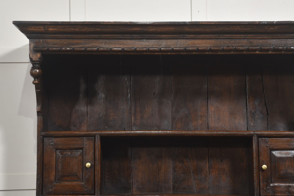An antique dark oak Welsh dresser featuring an upper open shelf rack with two small side cupboards over a three-drawer base with two arched panel doors. View XII