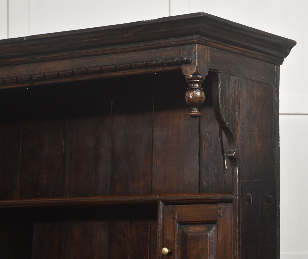 An antique dark oak Welsh dresser featuring an upper open shelf rack with two small side cupboards over a three-drawer base with two arched panel doors. View XVI