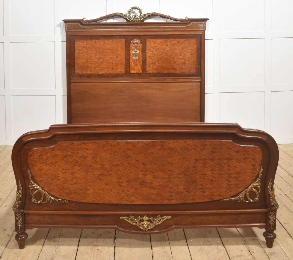 A Louis XVI style mahogany double bed frame featuring decorative parquetry veneer panels and polished gilt bronze mounts.