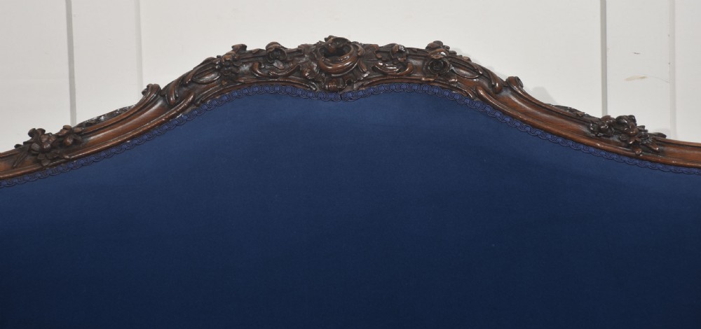 A 19th-century carved walnut settee featuring deep blue velvet upholstery, a serpentine crest rail, and hand-carved cabriole legs on small castors. View II