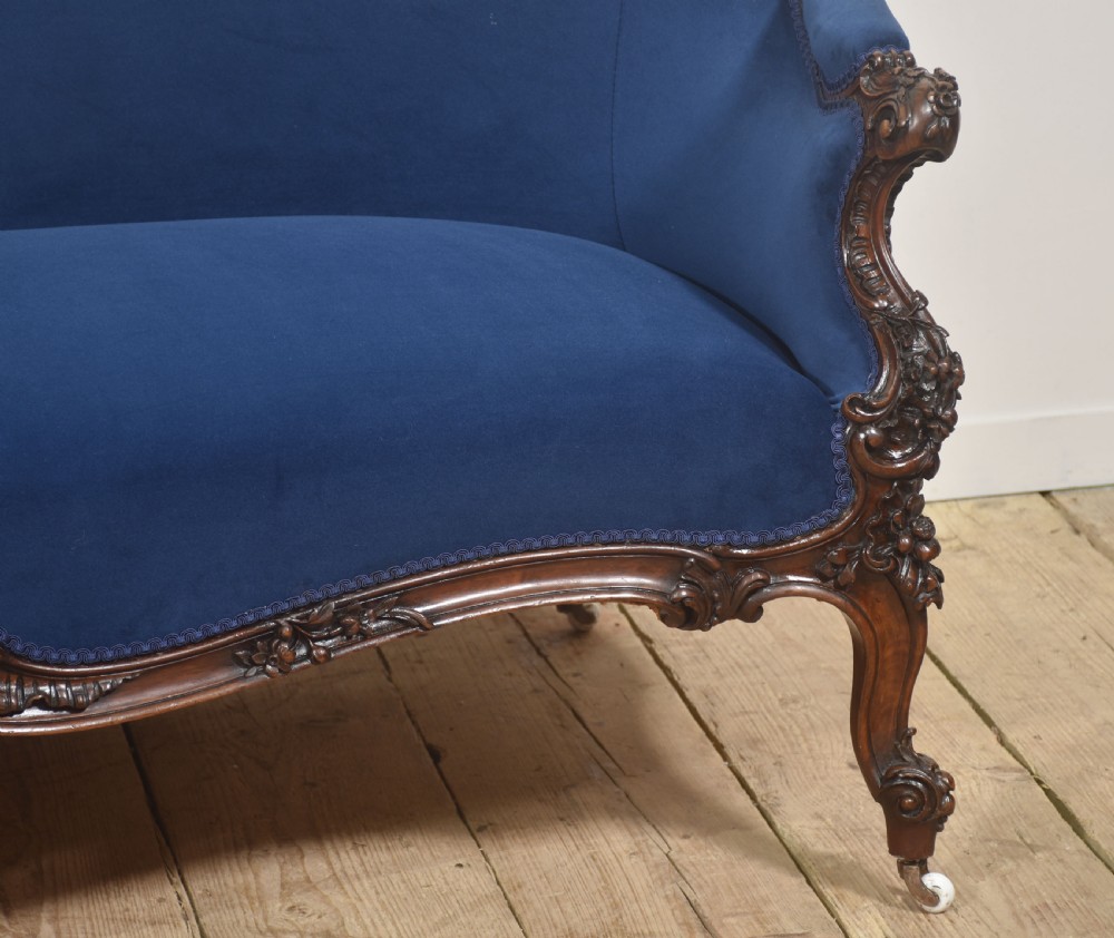 A 19th-century carved walnut settee featuring deep blue velvet upholstery, a serpentine crest rail, and hand-carved cabriole legs on small castors. View IV