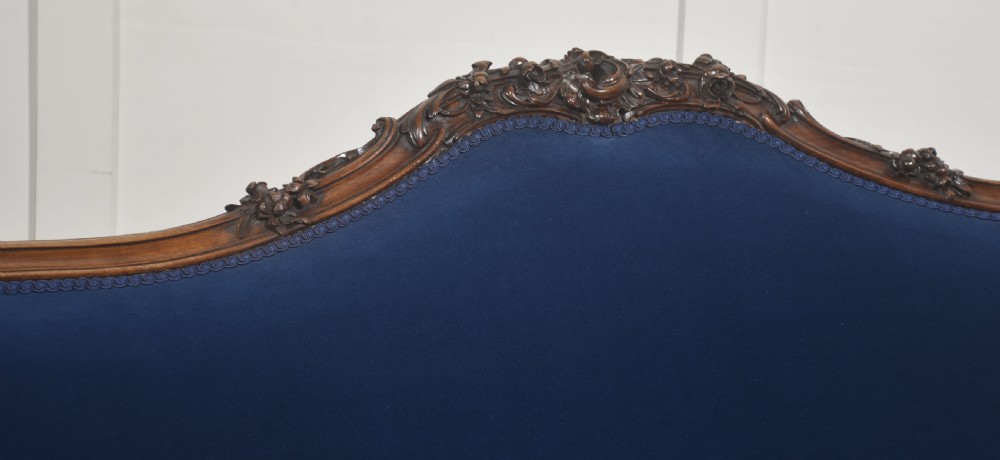 A 19th-century carved walnut settee featuring deep blue velvet upholstery, a serpentine crest rail, and hand-carved cabriole legs on small castors. View IX