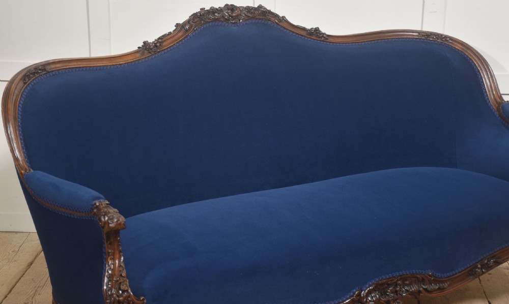 A 19th-century carved walnut settee featuring deep blue velvet upholstery, a serpentine crest rail, and hand-carved cabriole legs on small castors. View XII