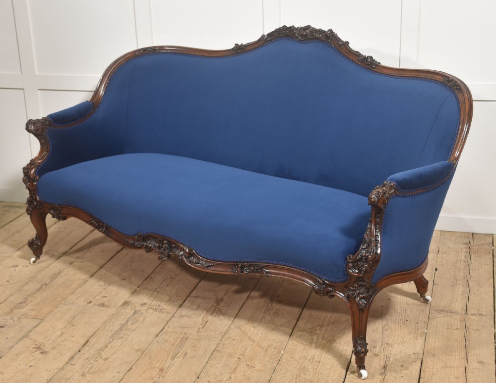 A 19th-century carved walnut settee featuring deep blue velvet upholstery, a serpentine crest rail, and hand-carved cabriole legs on small castors. View XIII