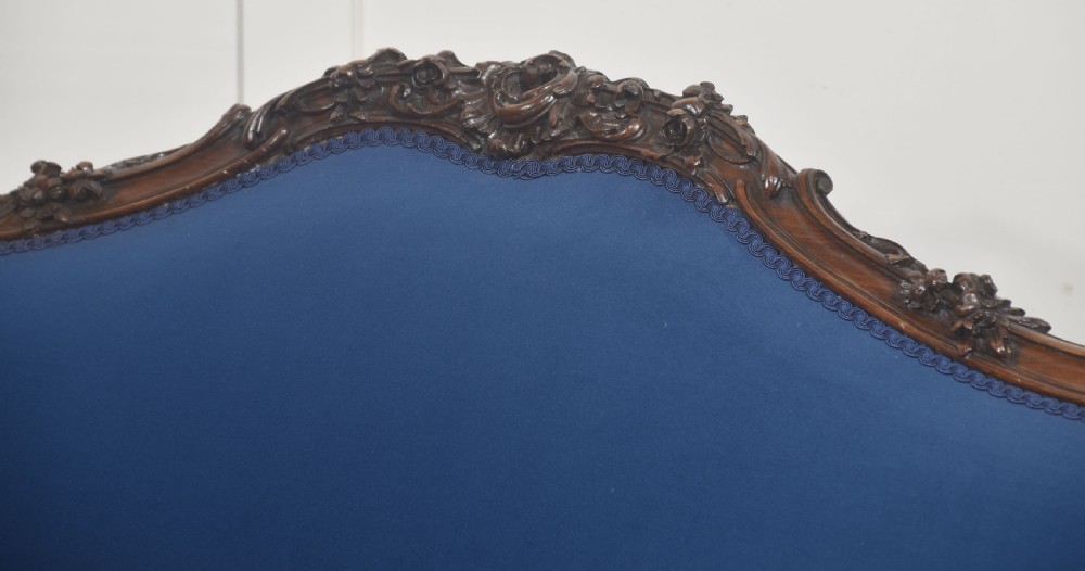A 19th-century carved walnut settee featuring deep blue velvet upholstery, a serpentine crest rail, and hand-carved cabriole legs on small castors. View XIV