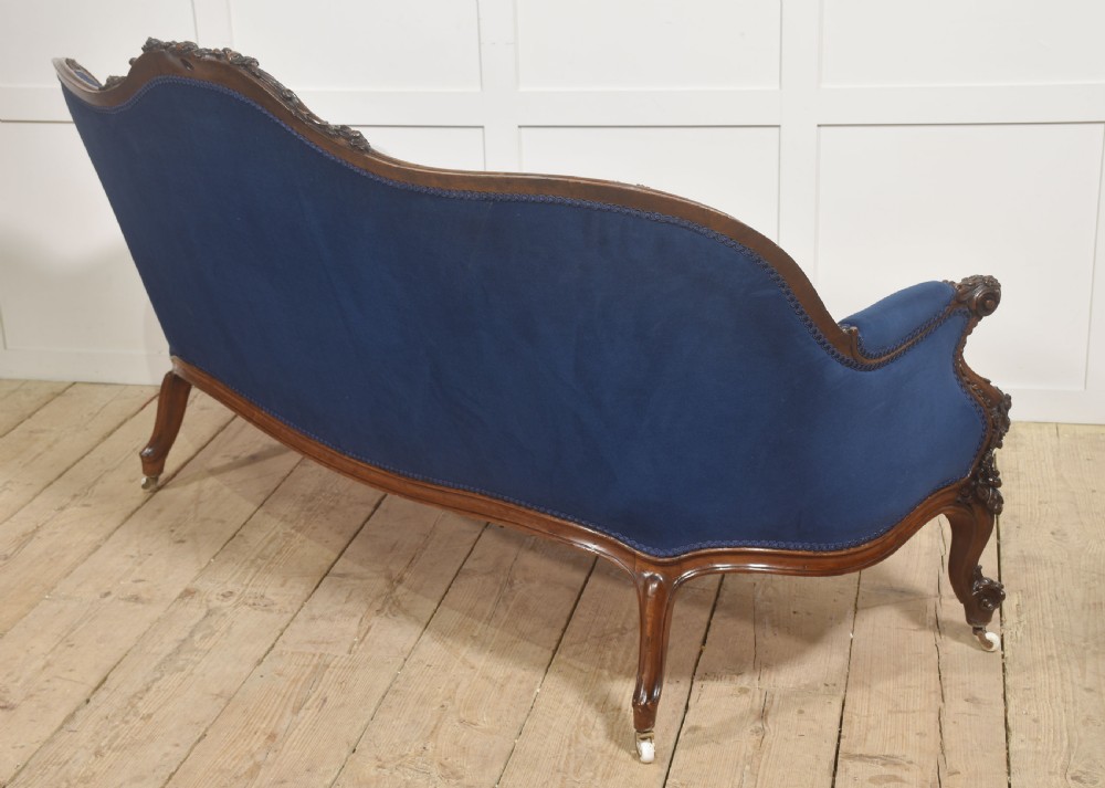 A 19th-century carved walnut settee featuring deep blue velvet upholstery, a serpentine crest rail, and hand-carved cabriole legs on small castors. View XV