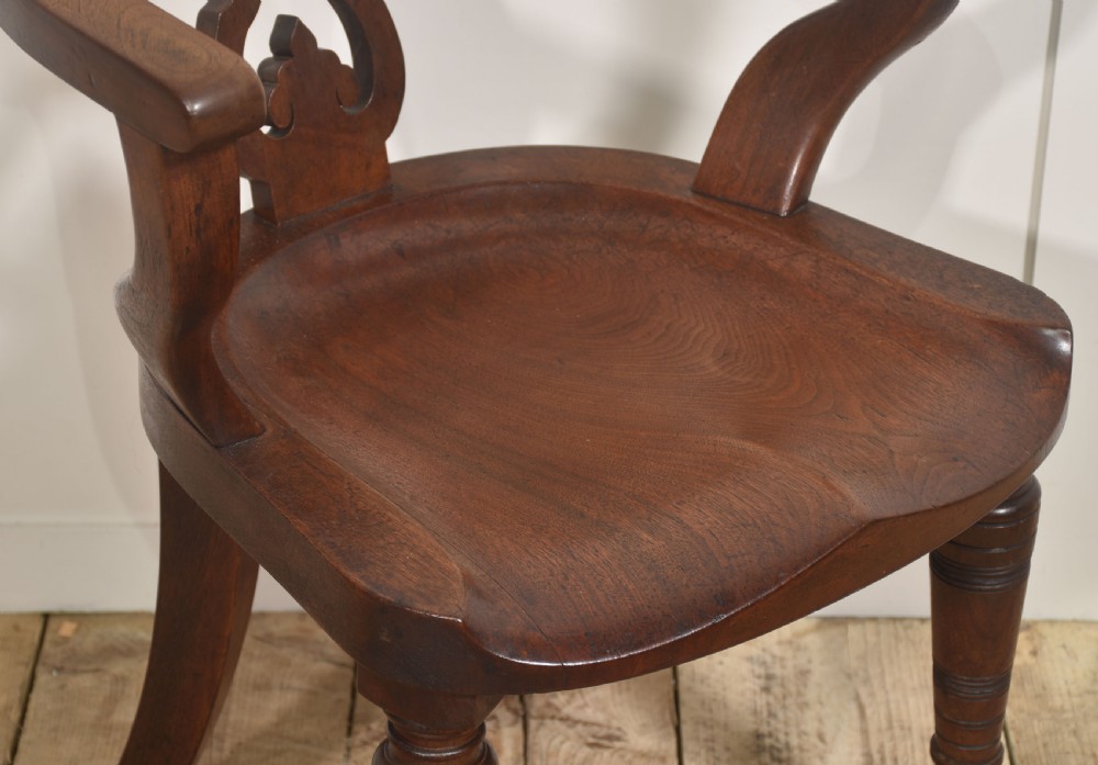 An antique dark walnut desk armchair featuring a curved horseshoe backrest, carved back splat, contoured seat, and turned front legs on brass castors. View V