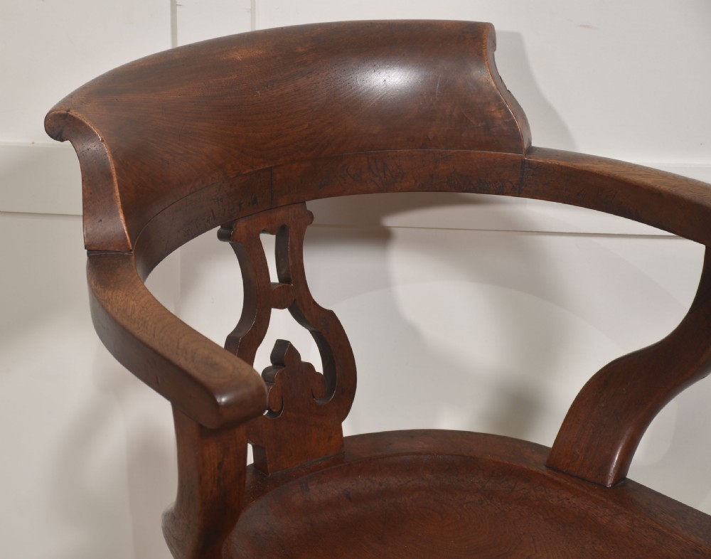 An antique dark walnut desk armchair featuring a curved horseshoe backrest, carved back splat, contoured seat, and turned front legs on brass castors. View VI