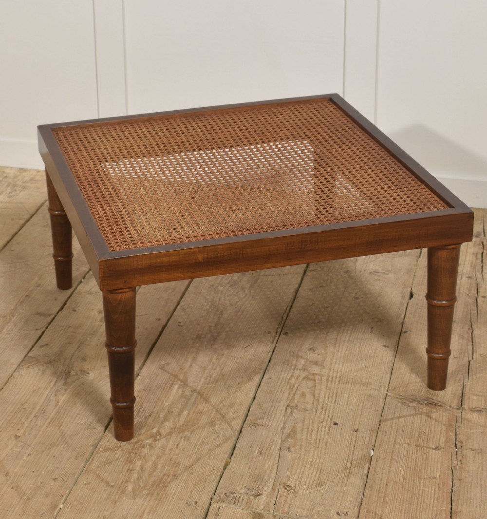 A square mahogany coffee table featuring a woven cane top set within a solid wood frame and supported by turned legs. View VI